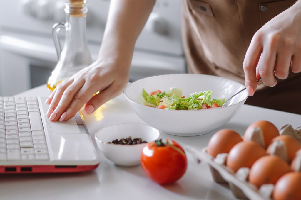 Woman prepares dietary vegetable salad at home using video recipe. Online cooking lessons